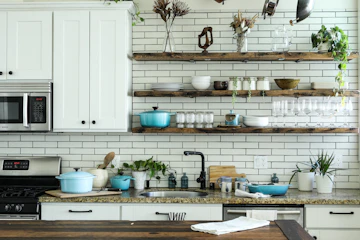 Compact white kitchen with subway tile, open wooden shelves, cabinets, and cookware.