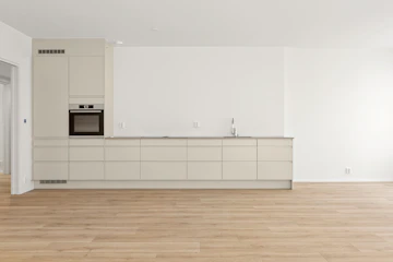 Empty apartment kitchen and living room with oven, cabinets, sink, microwave, appliances, and sideboard.