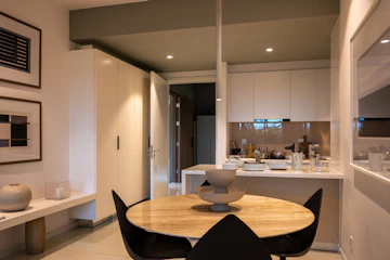 Apartment dining and living interior with brown wooden table, chair, sink, doorway, and plywood flooring.