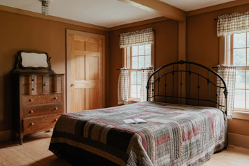 Warm-toned bedroom with bed, wood furniture, curtains, blanket, and natural light.