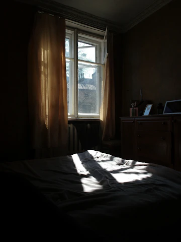 Bedroom with bed, paired windows, wood floor, and dorm-room style furnishings.