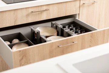 Organized kitchen drawer with dishes, spices, plates, mugs, cups, and wood cabinetry.