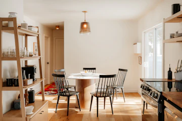 Dining area with wooden table, chairs, kitchen island, oven, and natural light.