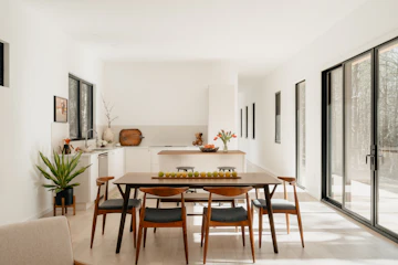 Modern dining area connected to a kitchen, with table, chairs, white walls, and natural light.