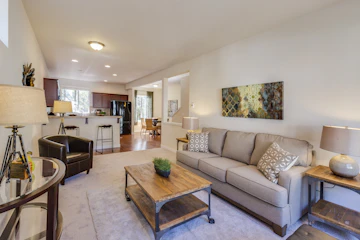 Staged living-room interior with sofa, chair, lamp, coffee table, and bar stools.