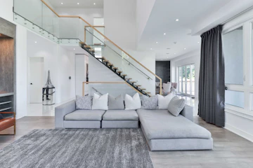 Modern minimalist living room with rug, cushions, furniture, and staircase.