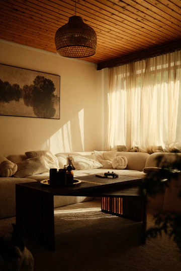 Warm living room with sofa, teak table, curtains, cushions, and natural light.